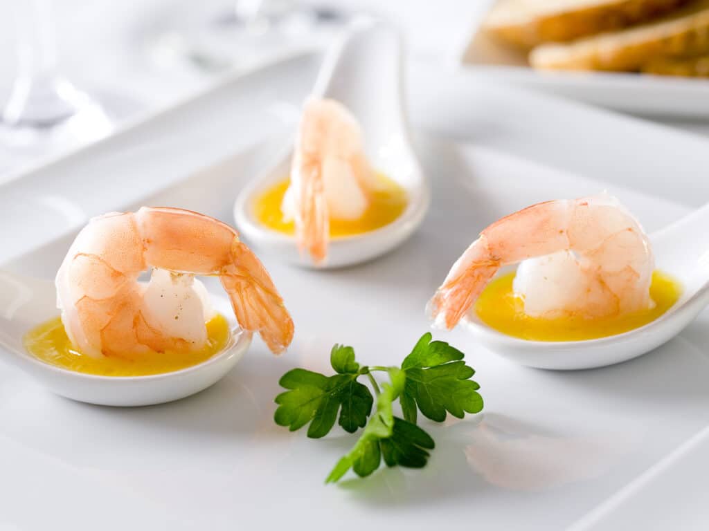 Three shrimp and orange sauce gourmet appetizers on spoons.