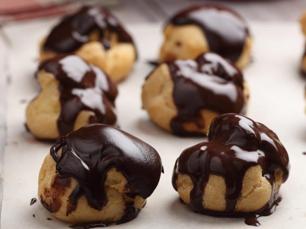 Rows of Profiteroles with chocolate glaze on a baking paper