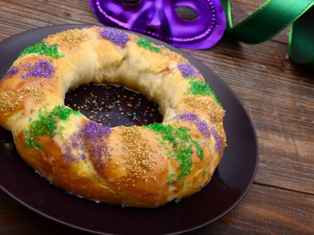 A traditional round King Cake for Mardi Gras decorated with purple, gold, and green sugar sprinkles.