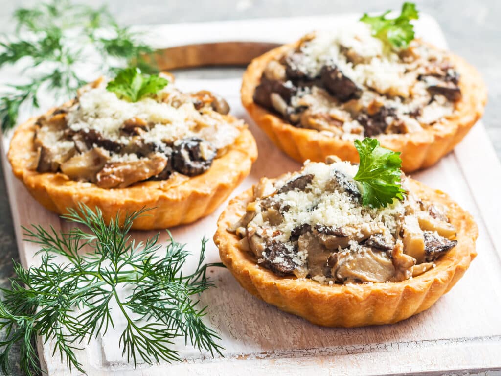 Homemade savory autumn tarts with fresh seasonal mushrooms in a crisp pastry base on gray background