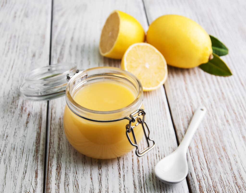Lemon curd in glass jar with fresh lemons on a old wooden table