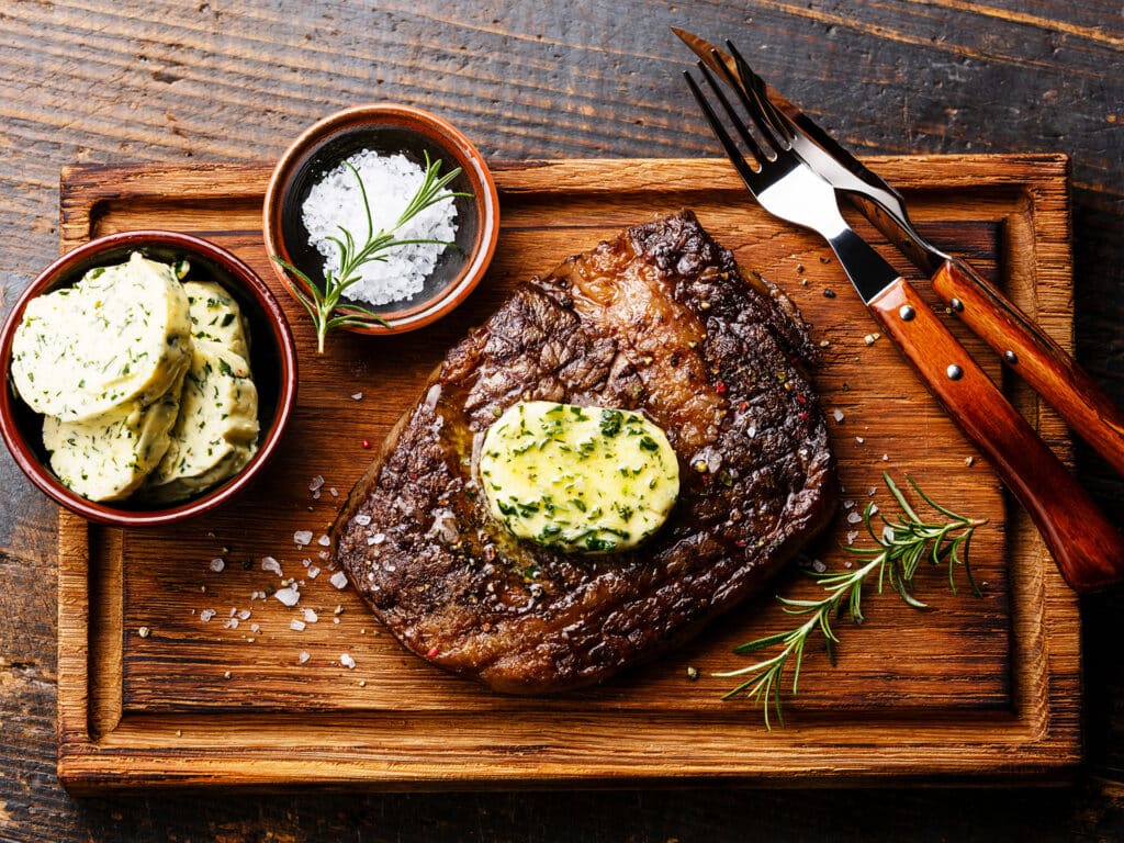Sliced grilled steak Ribeye with herb butter on cutting board on wooden background