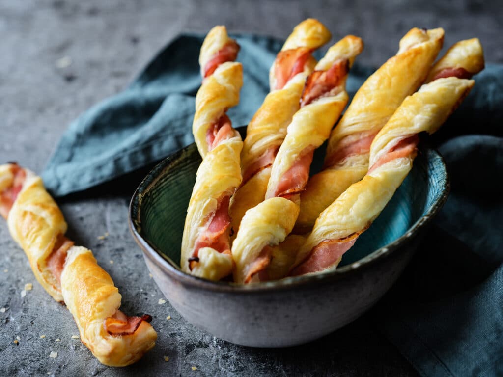 Twisted puff pastry sticks with bacon slices
