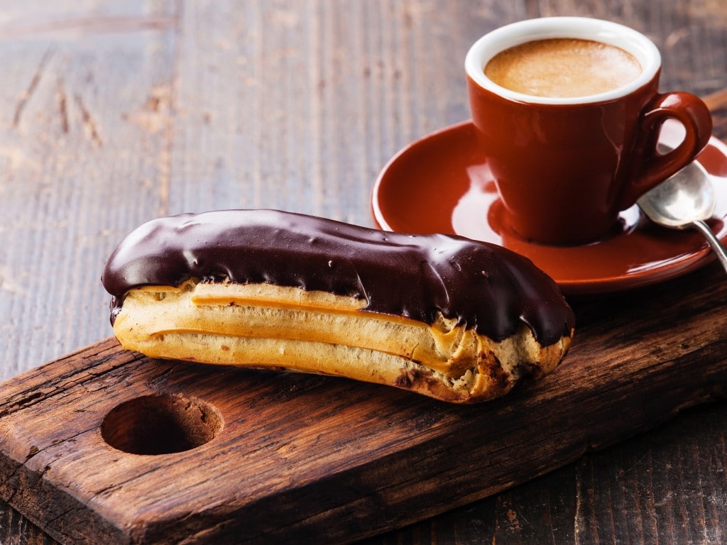 Chocolate eclair and coffee cup on dark wooden background