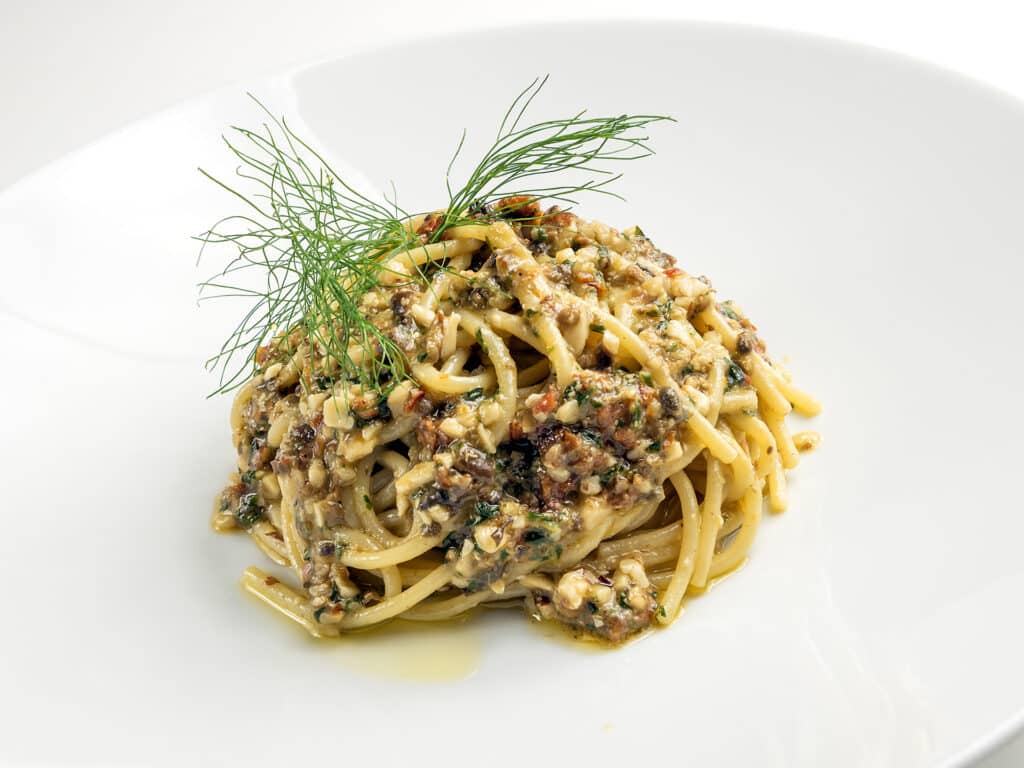 Dish of spaghetti with sauce of capers olives pine nuts dried tomatoes minced on white background