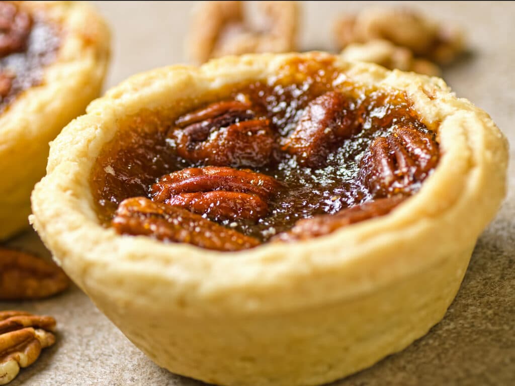 Two pecan tarts with pecans set against a simple background.