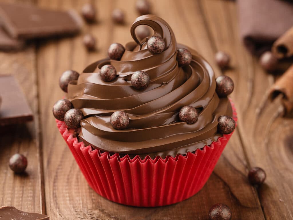 Homemade chocolate cupcake with chocolate chips in red cup on wooden background with cinnamon and sprinkles