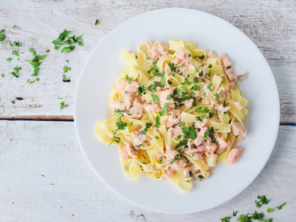 Italian Wholemeal Pasta Tagliatelle with Salmon and Parsley. Fresh pasta with smoked salmon in the sauce on white wooden background with place for text. Italian cuisine concept. Copy space. Top view.