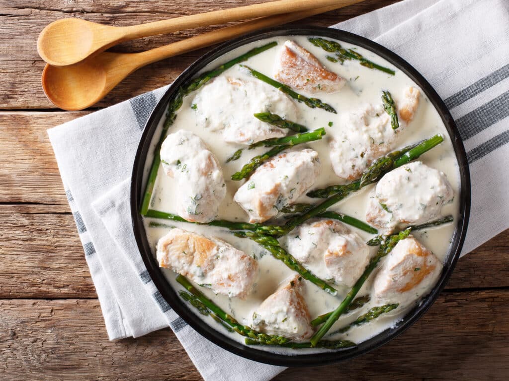 Pieces of chicken with baby asparagus in a creamy sauce close-up on a plate on a table. Horizontal top view from above
