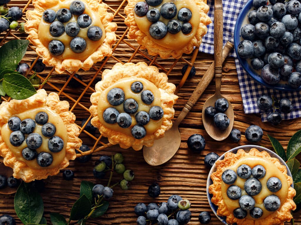 Small tarts made of puff pastry with addition fresh blueberries and caramel chocolate custard on a wooden rustic table, top view, close up. Delicious homemade dessert or breakfast