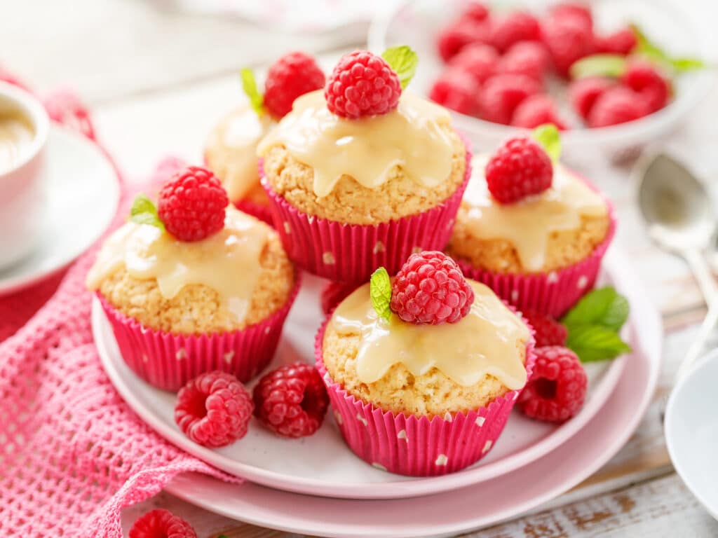 Cupcakes with white chocolate and fresh raspberries on a ceramic plate on a wooden white table, close-up. A delicious dessert or breakfast.