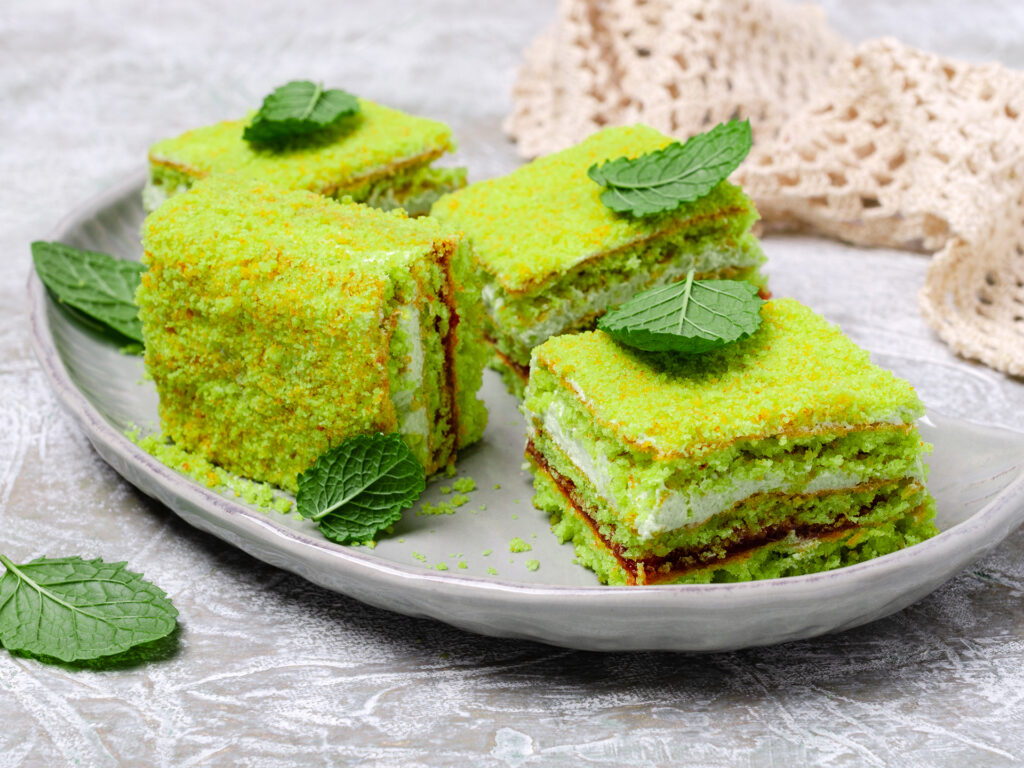 Traditional green sponge cake with cream and jam on slate background. Selective focus.