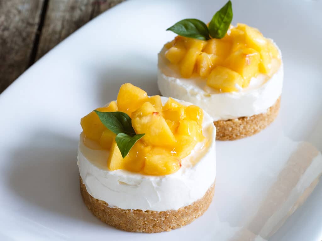 Mini cheesecake with peaches on wooden background.